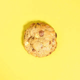 Biscoff New York Cookie with white and milk chocolate chips, Biscoff spread, crumbs, and Lotus biscuit chunks on yellow background.